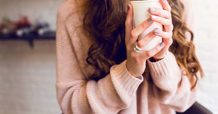 Image: a woman in a pink sweater holds a ceramic mug. 