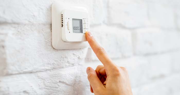 Image: a person's finger is adjusting a white thermostat. You can Run an Air Conditioner and Heater at the Same Time with the help of a thermostat.