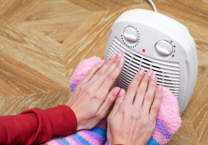 woman warming her hands and feet with a space heater